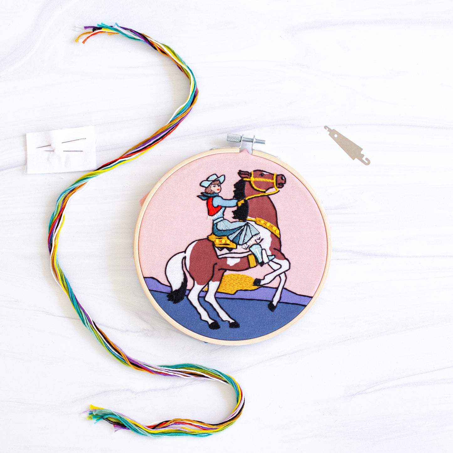 Embroidery kit with fabric, wooden hoop, thread, needle, and instructions for beginners, featuring a cowgirl riding a horse during sunset
