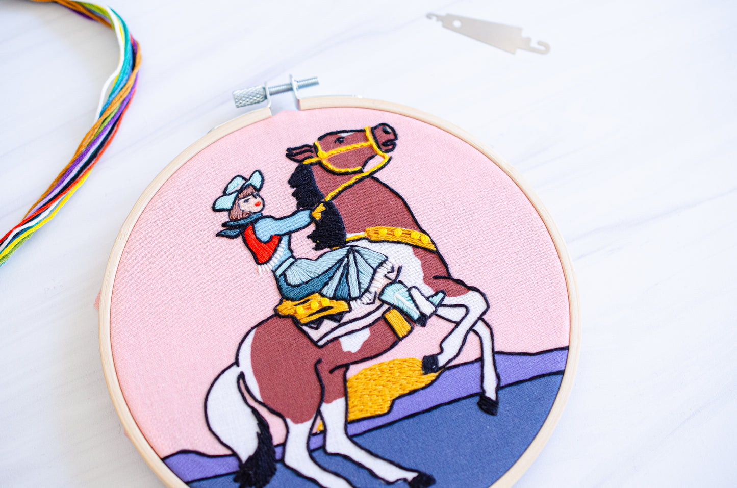 Embroidery kit with fabric, wooden hoop, thread, needle, and instructions for beginners, featuring a cowgirl riding a horse during sunset