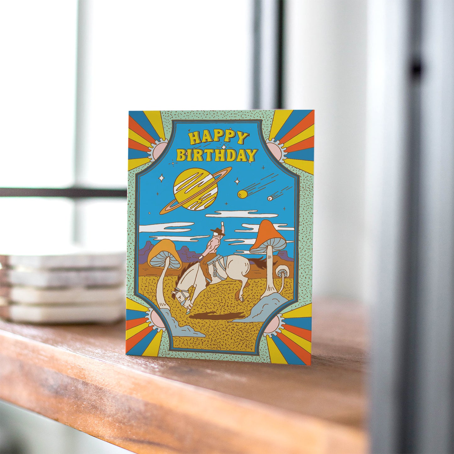 Psychedelic birthday card with cowboy on horseback in desert, giant mushrooms, ringed planet, and shooting stars.