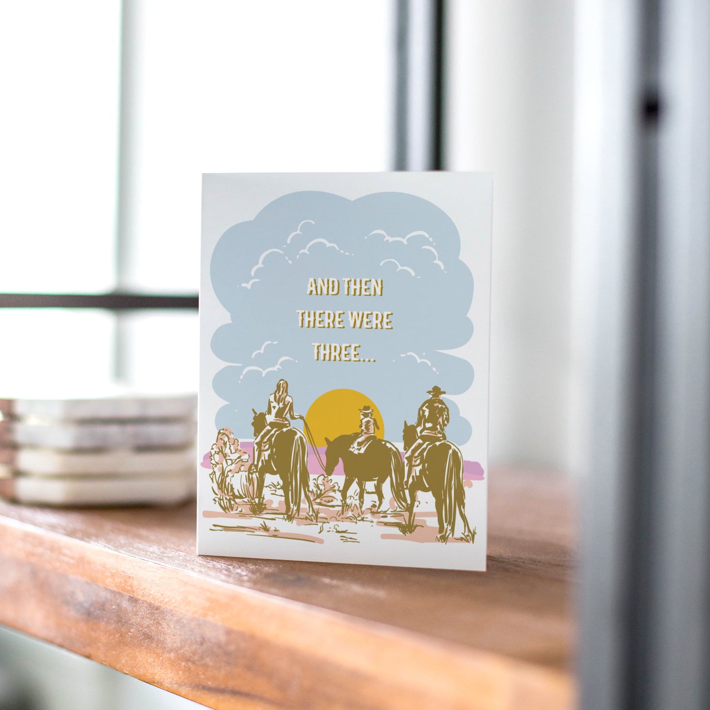 A beautifully illustrated greeting card featuring a desert landscape with two parents on horseback taking their little one on a trail ride. The warm, earthy tones capture the spirit of the Wild West, making it a perfect card for celebrating new babies, growing families, or Western-themed occasions