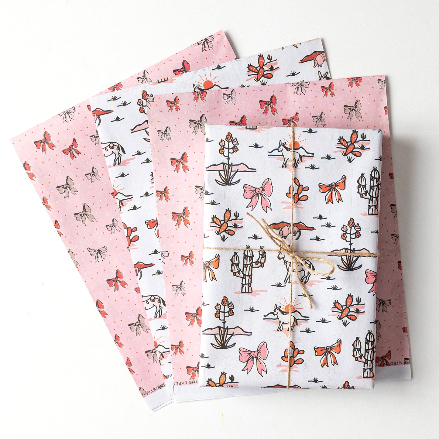 Double-sided sustainable gift wrap with cheerful desert themed holiday patterns on one side and holiday bows on the reverse, perfect for eco-friendly celebrations. 100% recyclable and compostable.