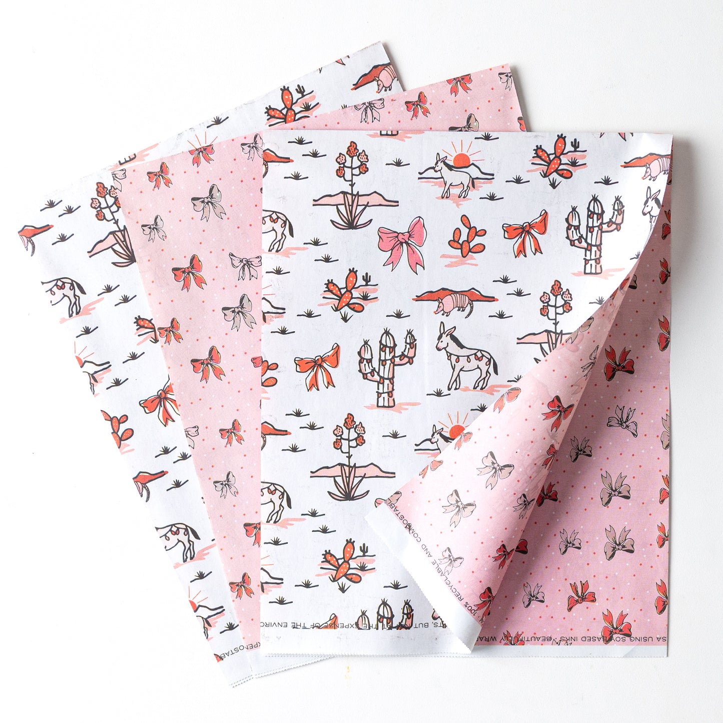Double-sided sustainable gift wrap with cheerful desert themed holiday patterns on one side and holiday bows on the reverse, perfect for eco-friendly celebrations. 100% recyclable and compostable.
