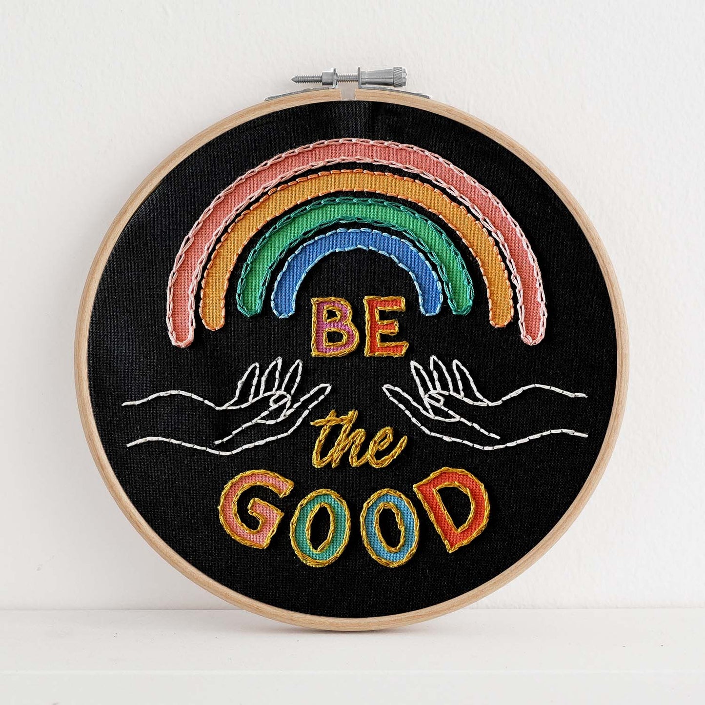 Embroidery kit with fabric, wooden hoop, thread, needle, and instructions for beginners, featuring a rainbow and the saying "be the good"