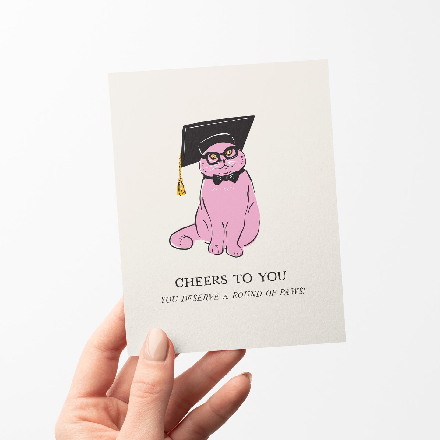 A stylish greeting card featuring a pink cat wearing a black graduation cap, glasses, and a bow tie. The card includes the message "Cheers to You" with the pun, "You deserve a round of paws!" Perfect for celebrating graduations and academic achievements.