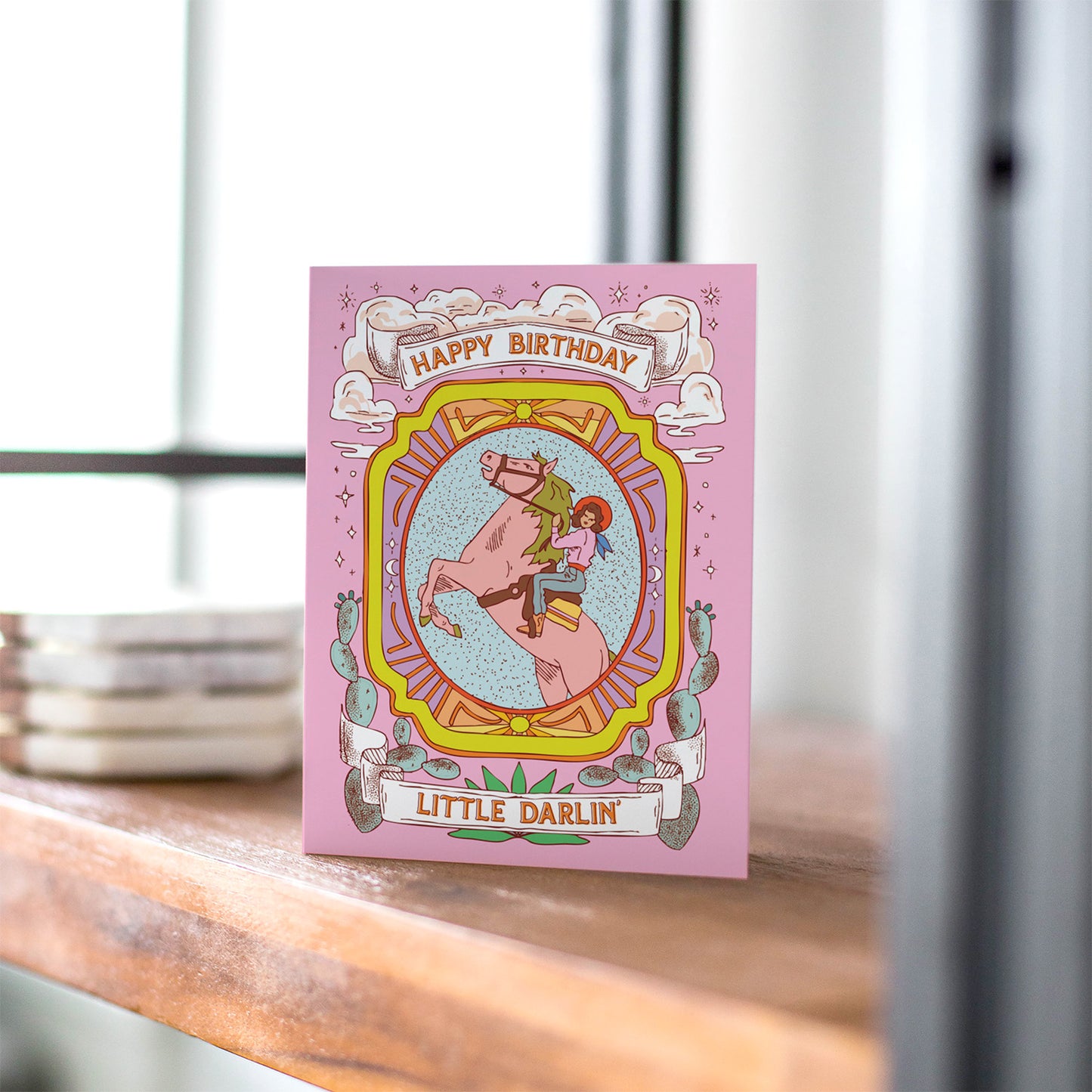 Western-themed pink birthday card with cowgirl riding a horse and the text “Happy Birthday Little Darlin’.”