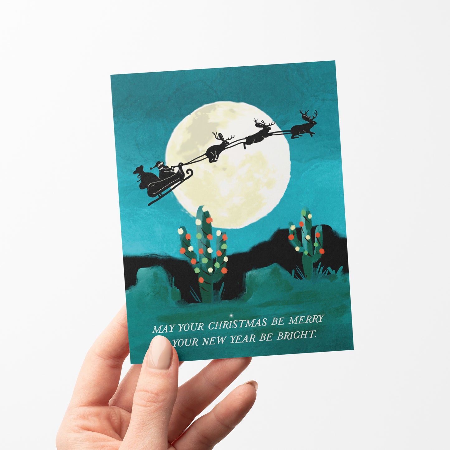 Jackelope Santa holiday card featuring jackelopes pulling Santa's slay across a full moon over a desert landscape, ideal for a unique holiday greeting, blank inside.
