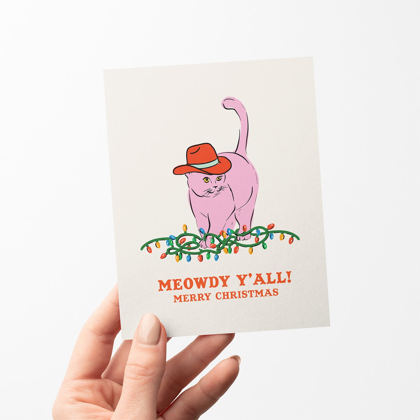 Christmas card with a pink cat wearing a red cowboy hat sitting on Christmas lights and the text “Meowdy Y’all! Merry Christmas.”