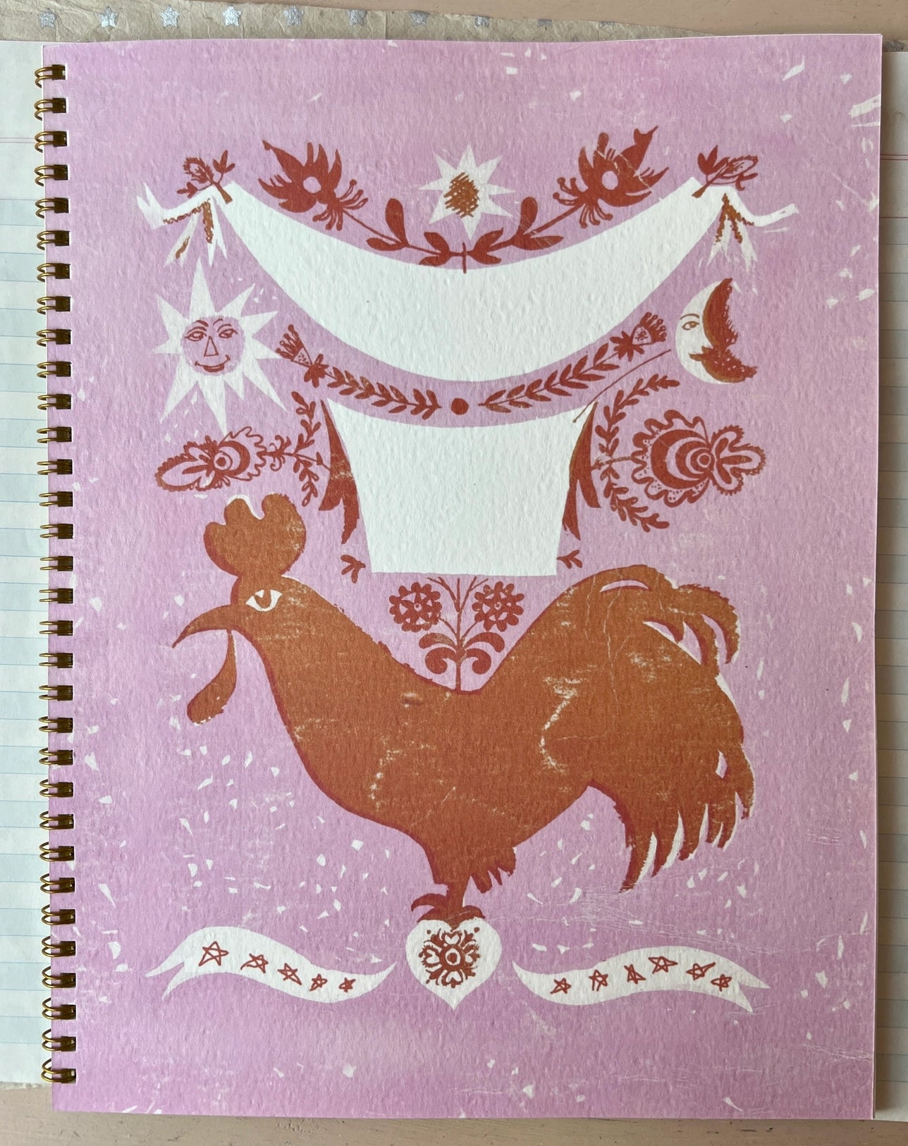 colorful softcover spiral-bound notebook featuring a rooster inspired design. lined interior pages.