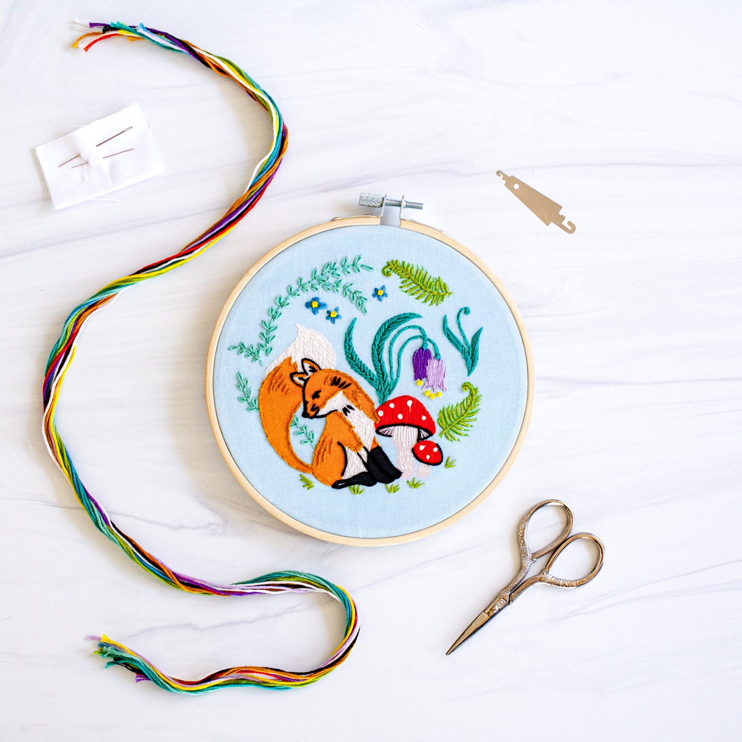 Embroidery kit with fabric, wooden hoop, thread, needle, and instructions for beginners, featuring cute fox surrounded by different flora and fauna 