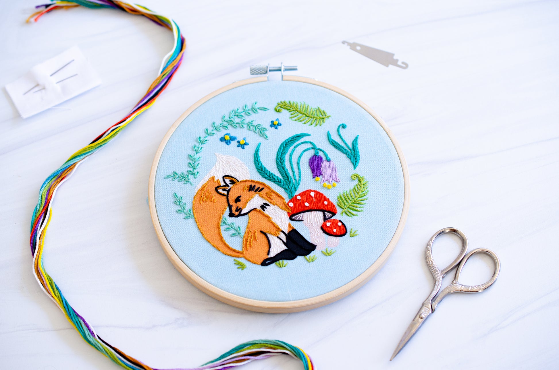 Embroidery kit with fabric, wooden hoop, thread, needle, and instructions for beginners, featuring cute fox surrounded by different flora and fauna 