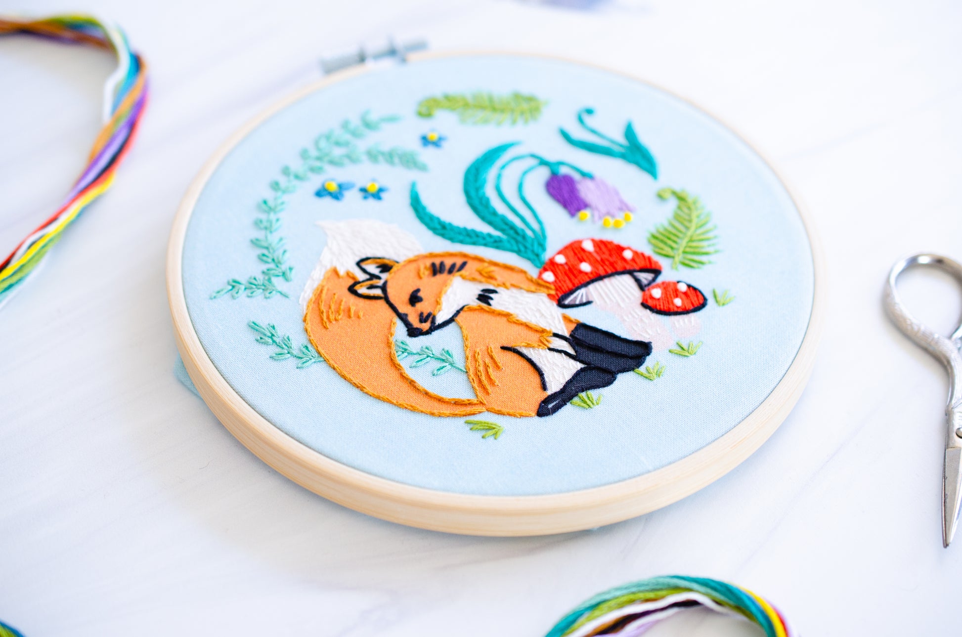 Embroidery kit with fabric, wooden hoop, thread, needle, and instructions for beginners, featuring cute fox surrounded by different flora and fauna 