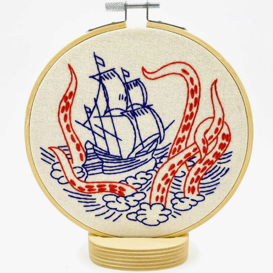 Embroidery kit with fabric, wooden hoop, thread, needle, and instructions for beginners, featuring a ship and kraken monster design.