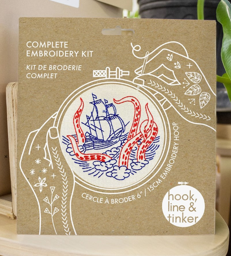 Embroidery kit with fabric, wooden hoop, thread, needle, and instructions for beginners, featuring a ship and kraken monster design.