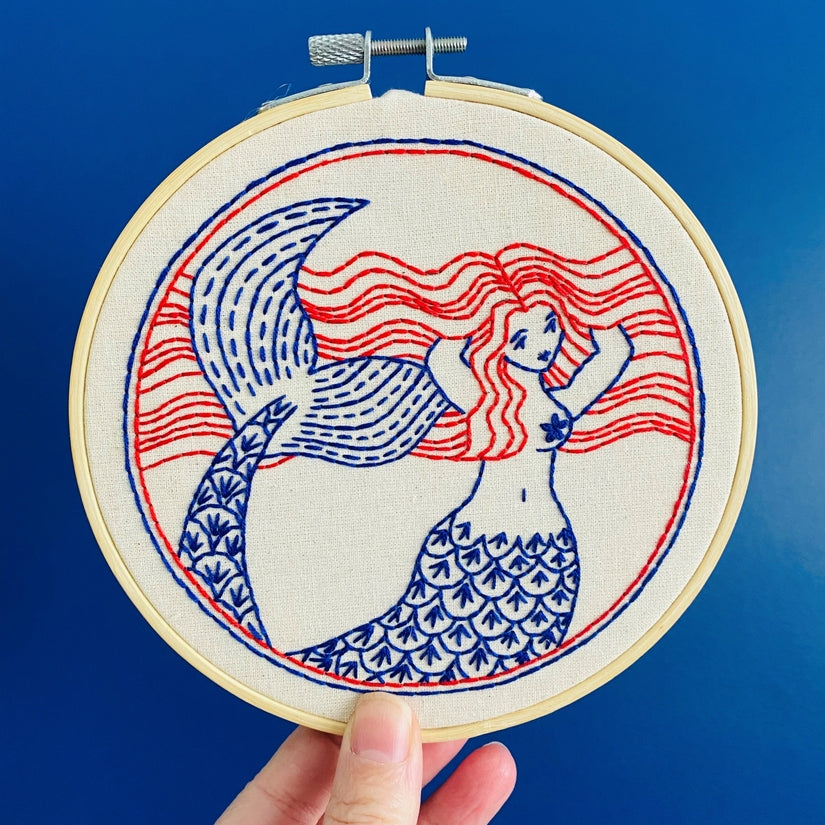 Embroidery kit with fabric, wooden hoop, thread, needle, and instructions for beginners, featuring a mermaid design.