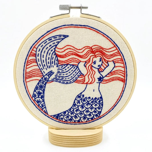 Embroidery kit with fabric, wooden hoop, thread, needle, and instructions for beginners, featuring a mermaid design.