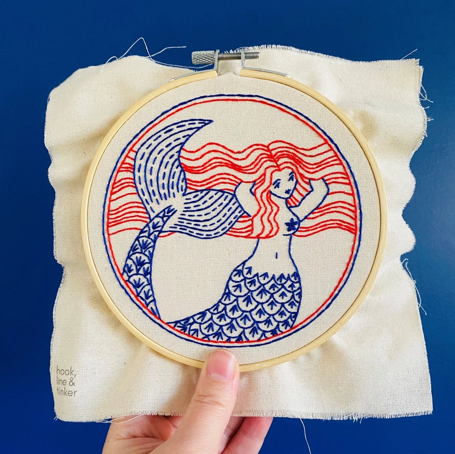 Embroidery kit with fabric, wooden hoop, thread, needle, and instructions for beginners, featuring a mermaid design.