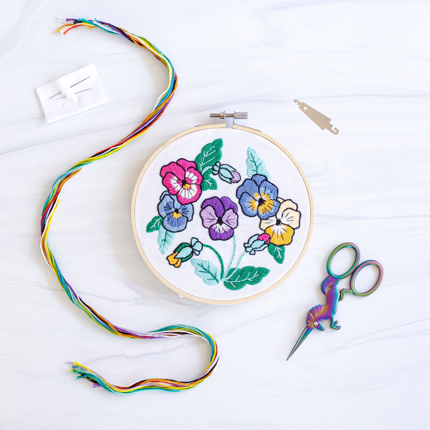 Embroidery kit with fabric, wooden hoop, thread, needle, and instructions for beginners, featuring brightly colored pansies
