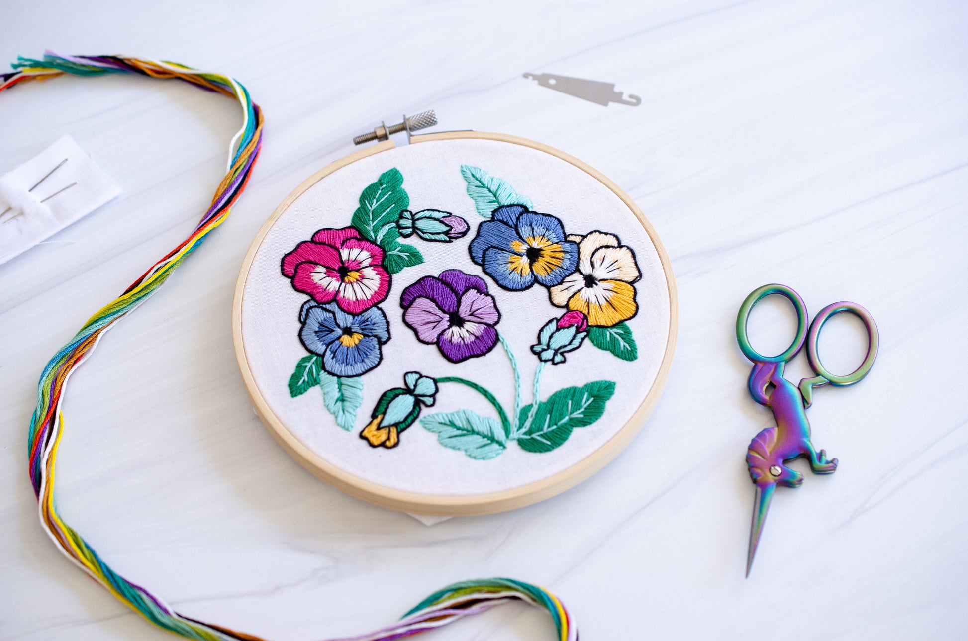 Embroidery kit with fabric, wooden hoop, thread, needle, and instructions for beginners, featuring brightly colored pansies