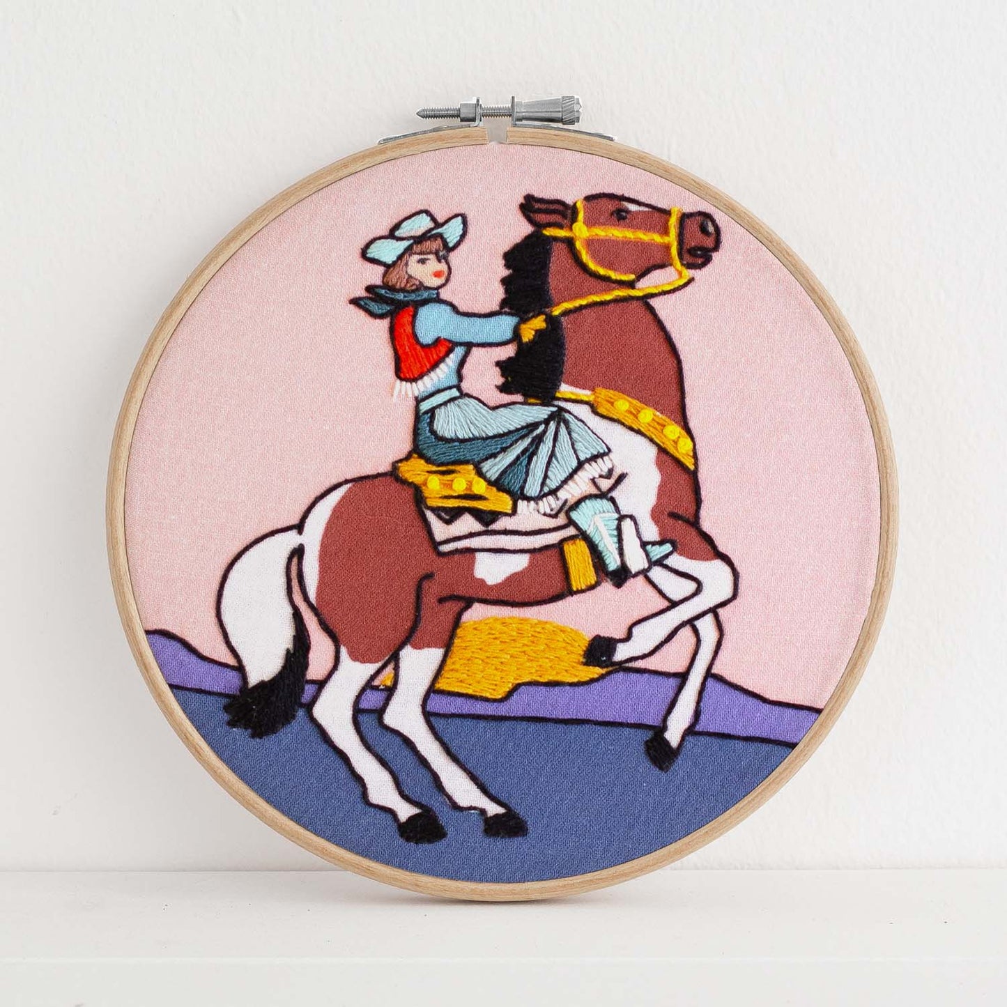 Embroidery kit with fabric, wooden hoop, thread, needle, and instructions for beginners, featuring a cowgirl riding a horse during sunset