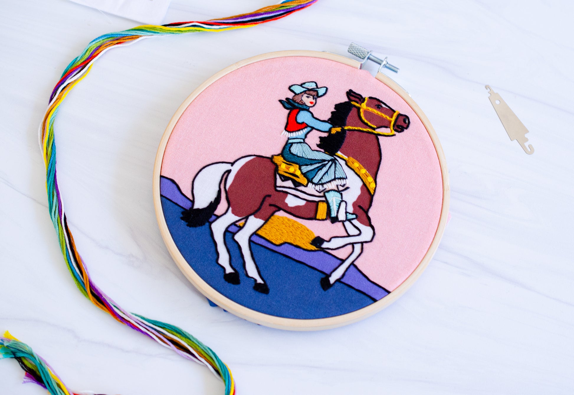 Embroidery kit with fabric, wooden hoop, thread, needle, and instructions for beginners, featuring a cowgirl riding a horse during sunset