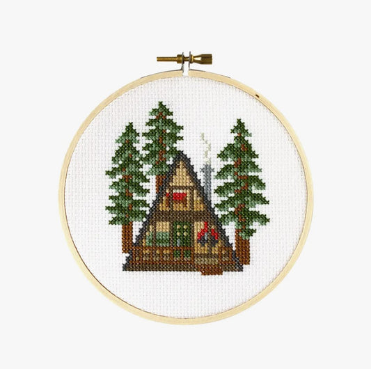 Cross stitch kit with fabric, wooden hoop, thread, needle, and instructions for beginners, featuring a cabin design.