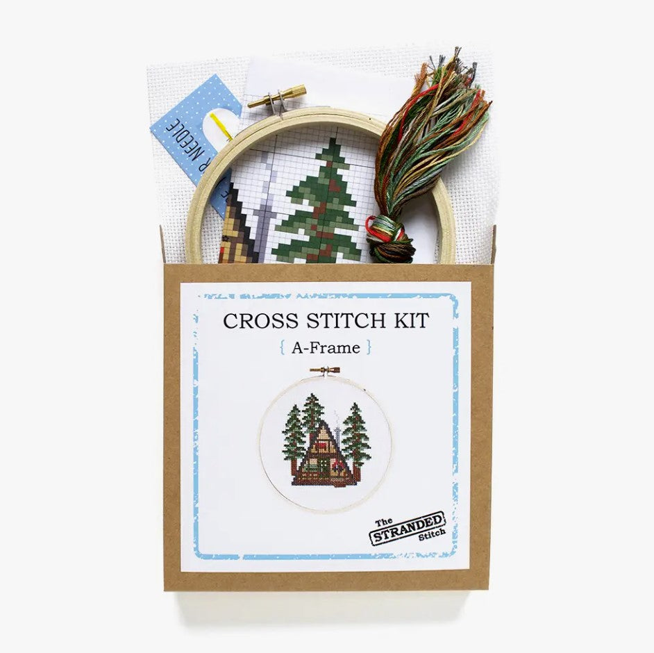 Cross stitch kit with fabric, wooden hoop, thread, needle, and instructions for beginners, featuring a cabin design.