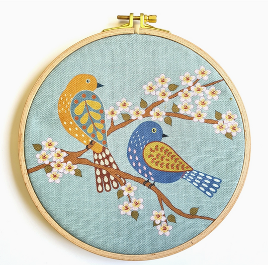 Embroidery kit with fabric, wooden hoop, thread, needle, and instructions for beginners, featuring a bird and blossom design.