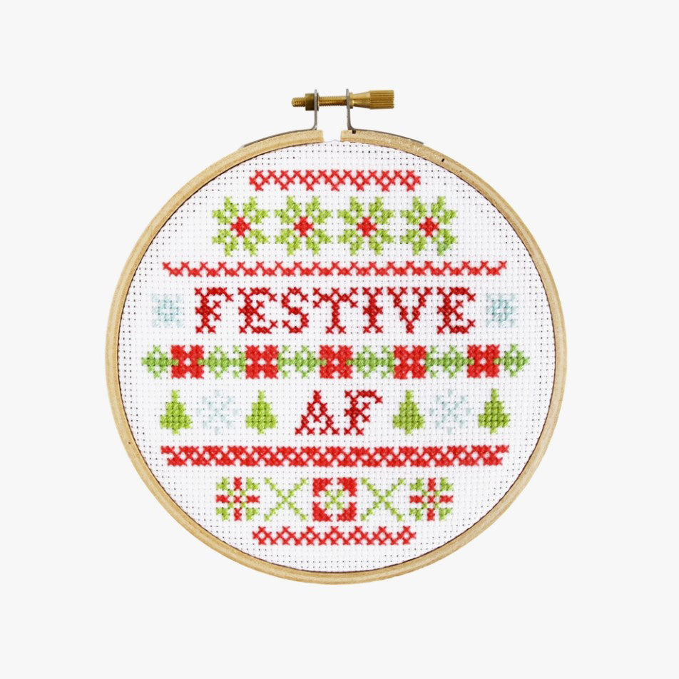 Cross stitch kit with fabric, wooden hoop, thread, needle, and instructions for beginners, featuring a festive saying design.