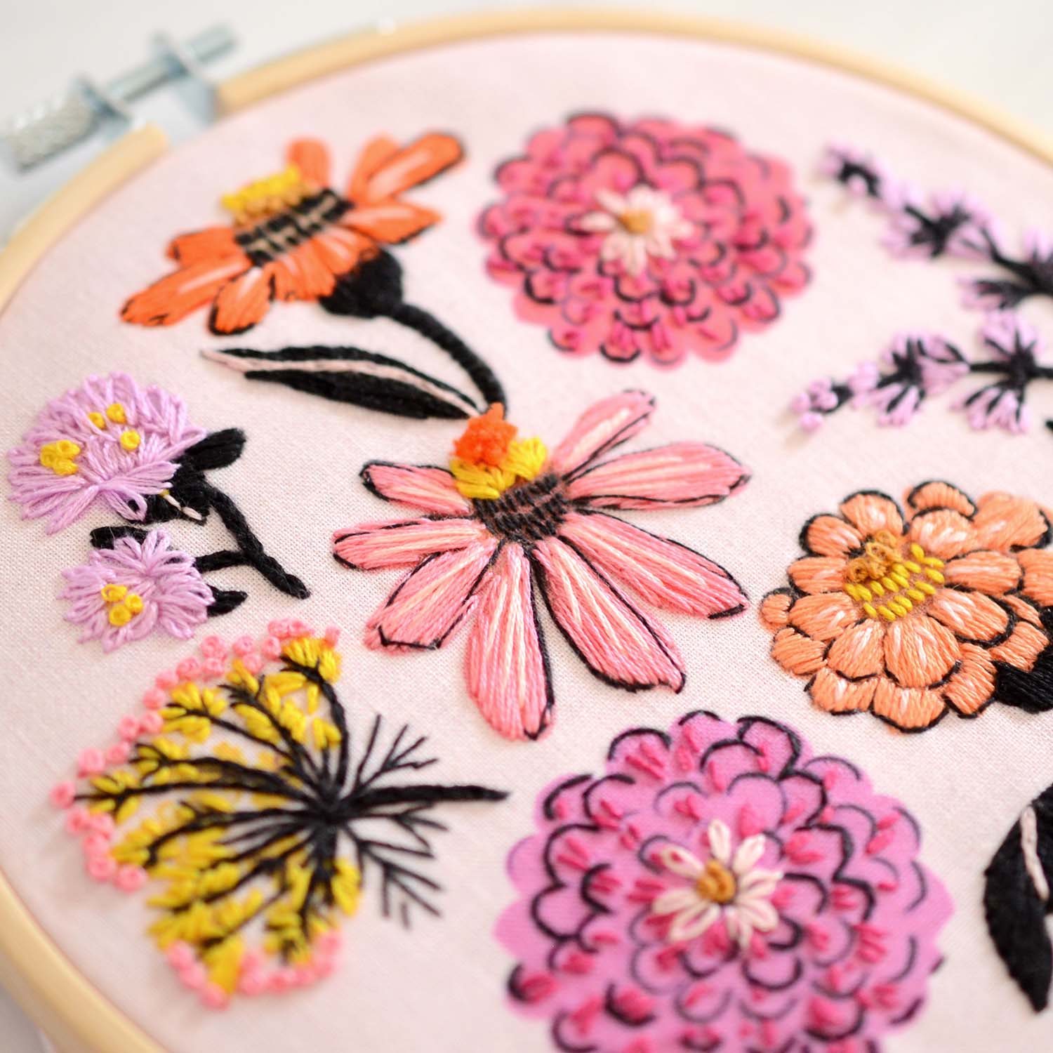 Embroidery kit with fabric, wooden hoop, thread, needle, and instructions for beginners, featuring brightly colored zinnia flowers