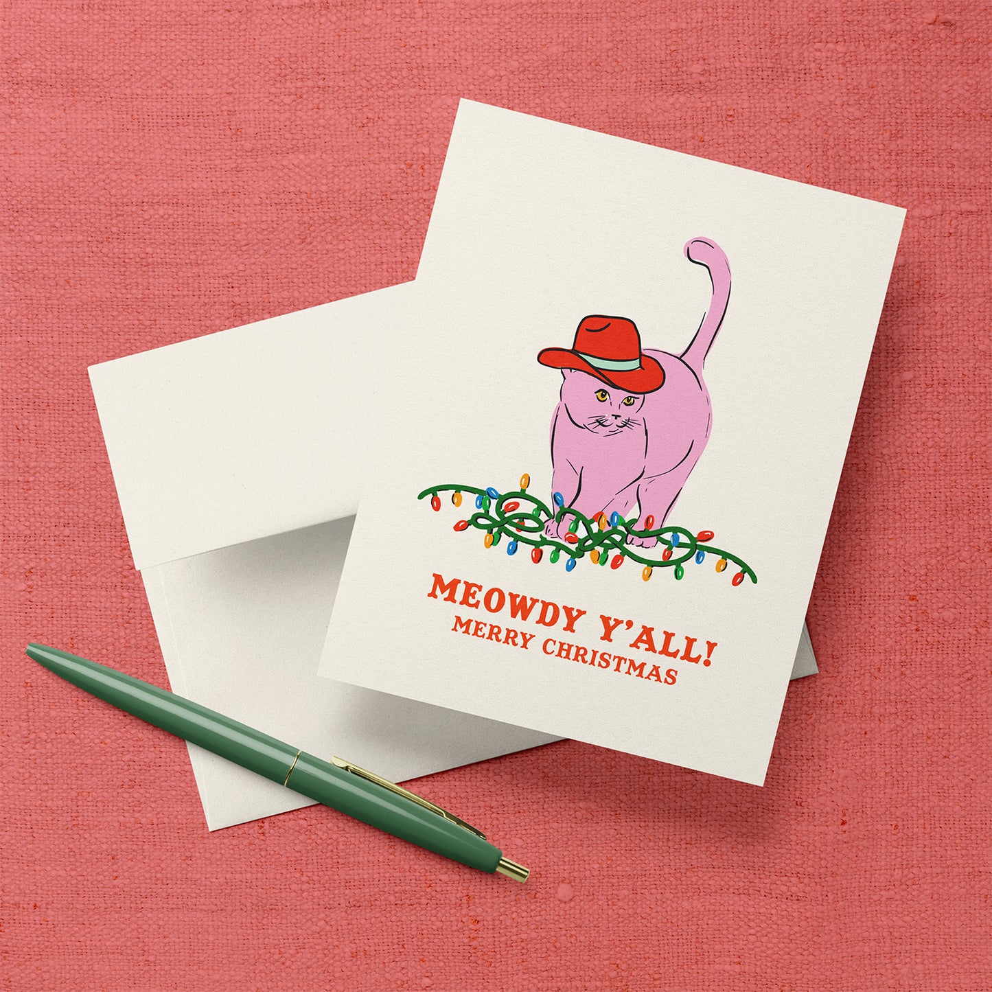 Christmas card with a pink cat wearing a red cowboy hat sitting on Christmas lights and the text “Meowdy Y’all! Merry Christmas.”