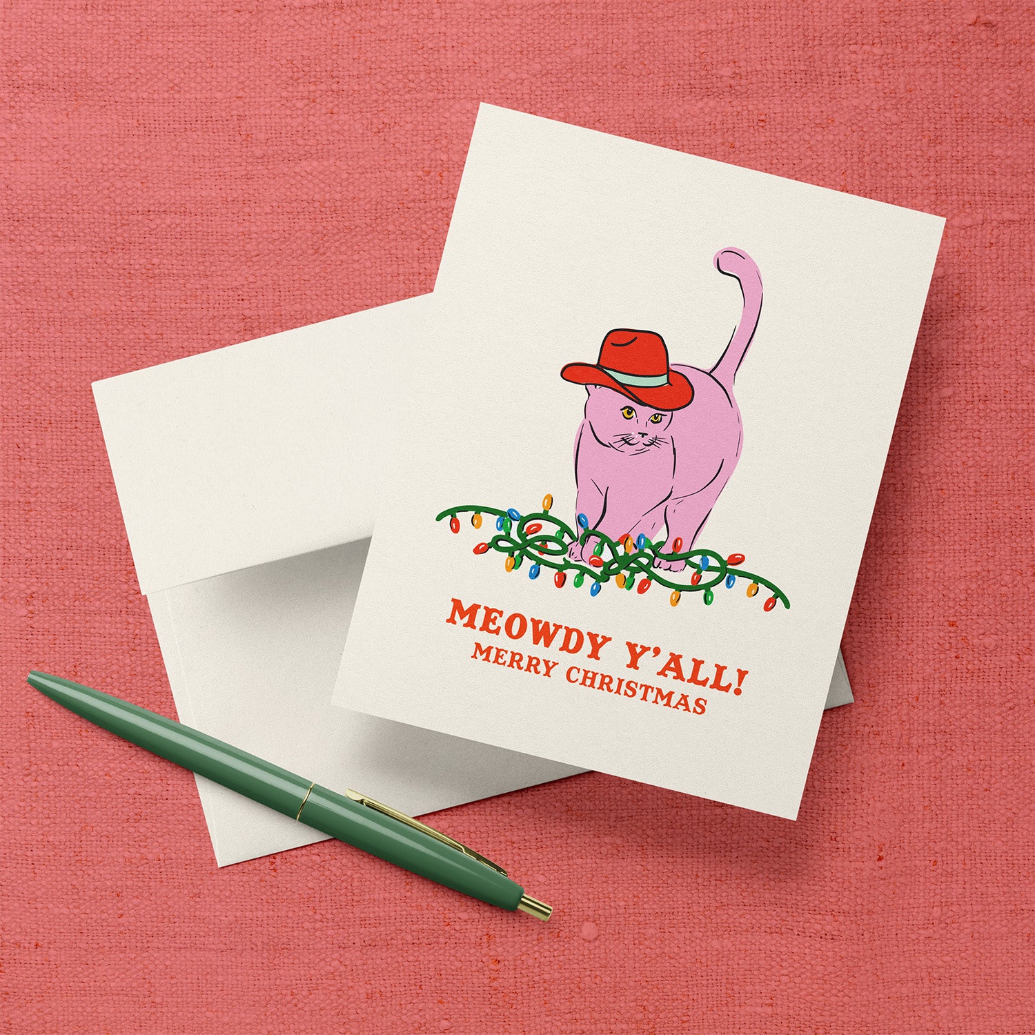 Christmas card with a pink cat wearing a red cowboy hat sitting on Christmas lights and the text “Meowdy Y’all! Merry Christmas.”