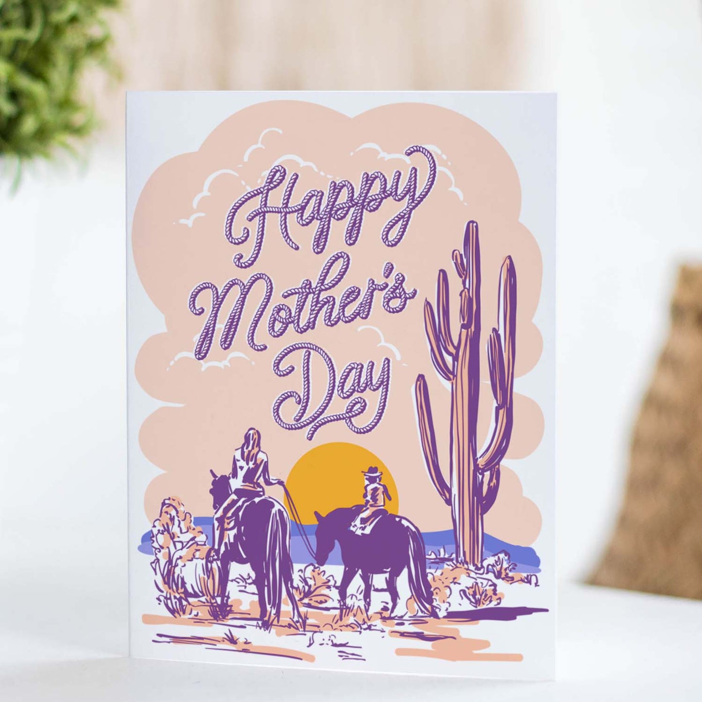 Mother’s Day card featuring an illustration of a mother and child on horses in a pastel desert landscape.