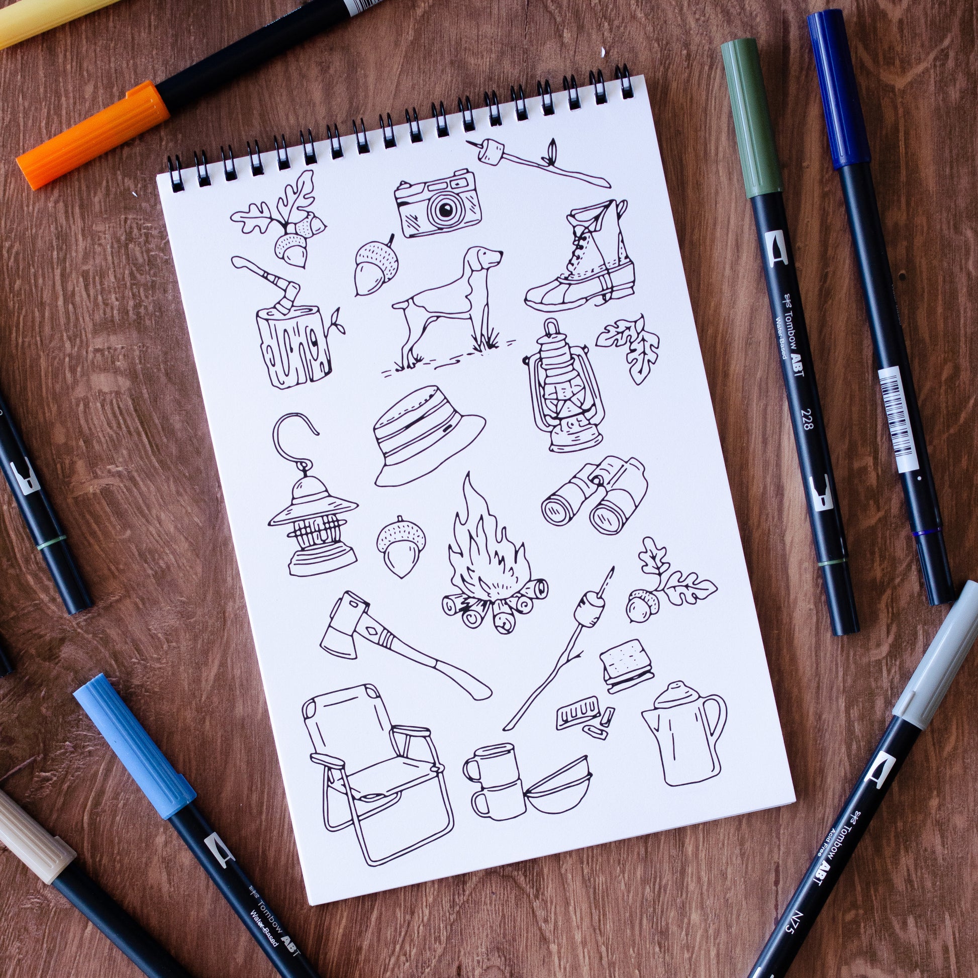 The Great Outdoors Coloring Book with 22 pages of hand-drawn nature illustrations featuring a camping scene, tent, pine trees, wildlife, and a cozy campfire under the stars. Spiral-bound adult coloring book for outdoor and adventure lovers.