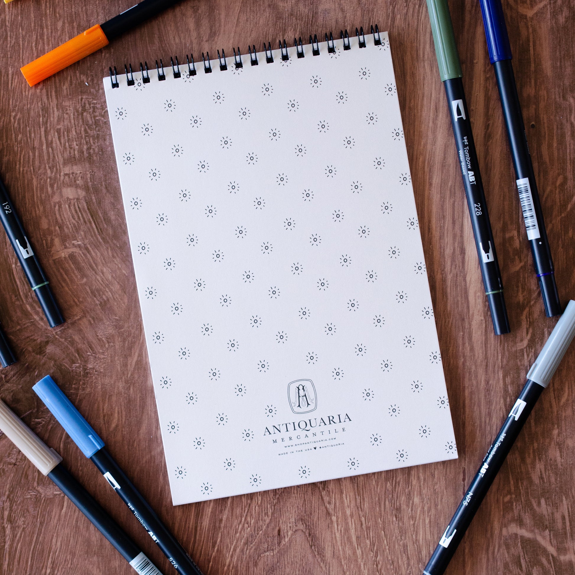 The Great Outdoors Coloring Book with 22 pages of hand-drawn nature illustrations featuring a camping scene, tent, pine trees, wildlife, and a cozy campfire under the stars. Spiral-bound adult coloring book for outdoor and adventure lovers.